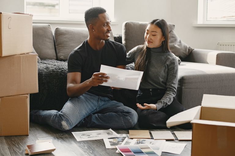 A happy couple plans home renovations surrounded by moving boxes and color samples.