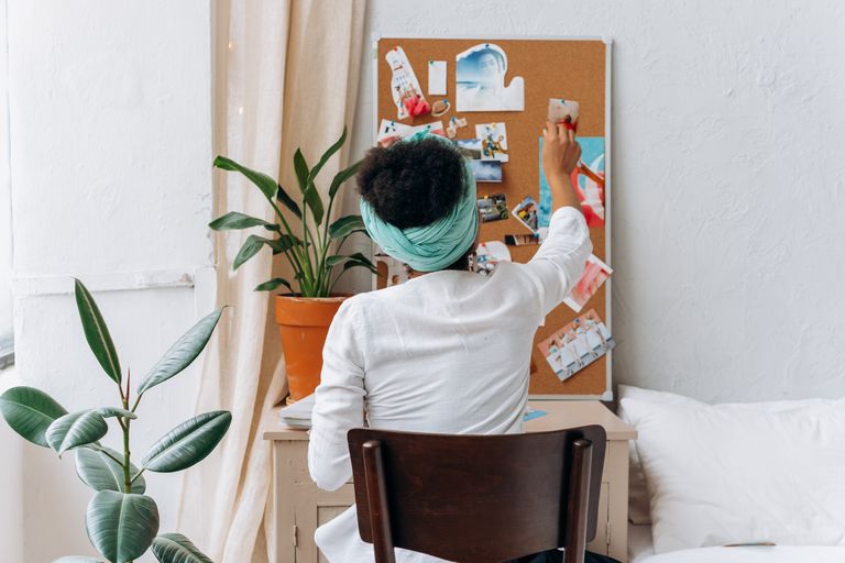A woman in a cozy room organizing a vision board with photos and ideas.